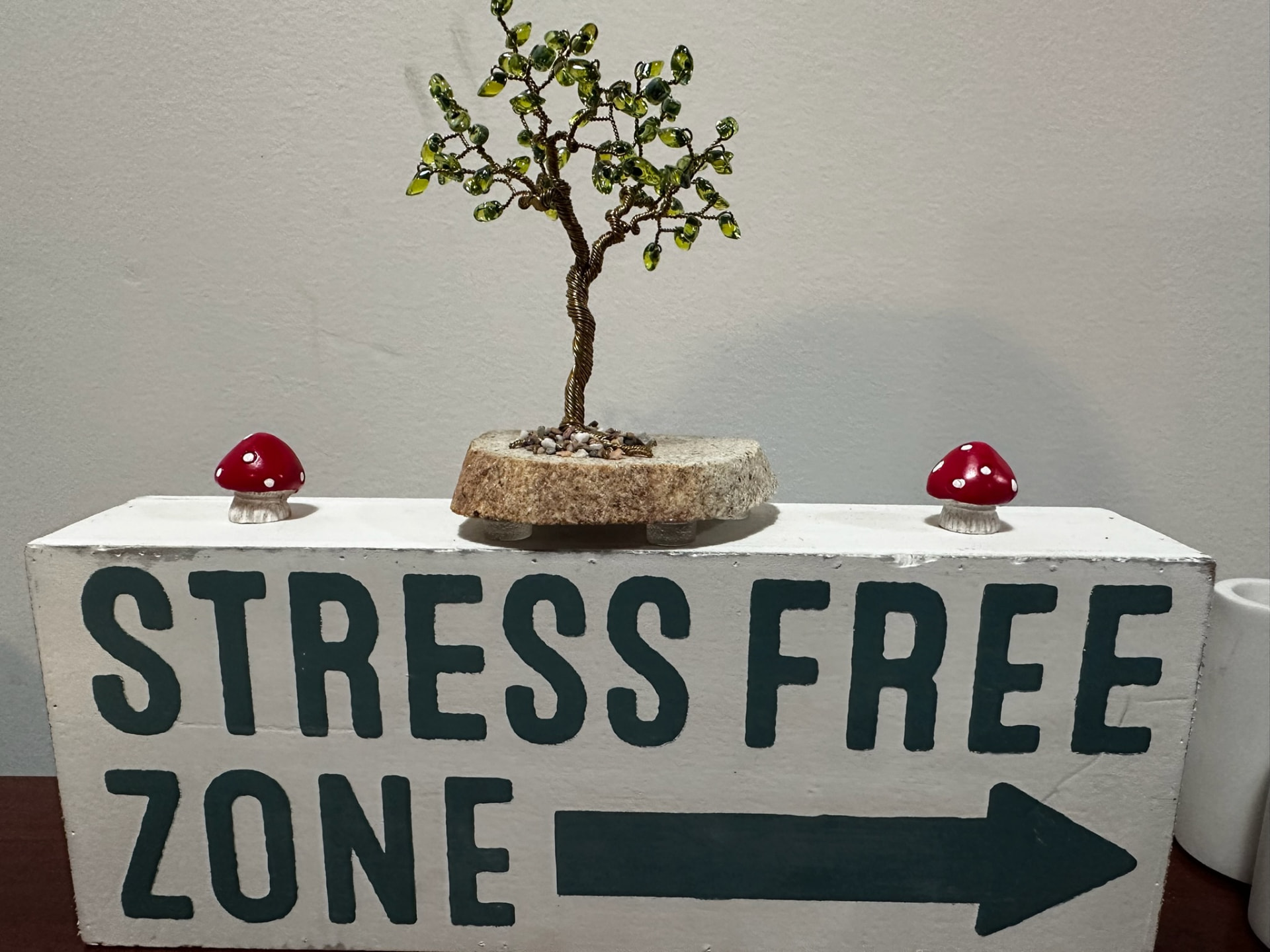 A hand-painted 'Stress Free Zone' sign with a beaded tree and small mushrooms on top