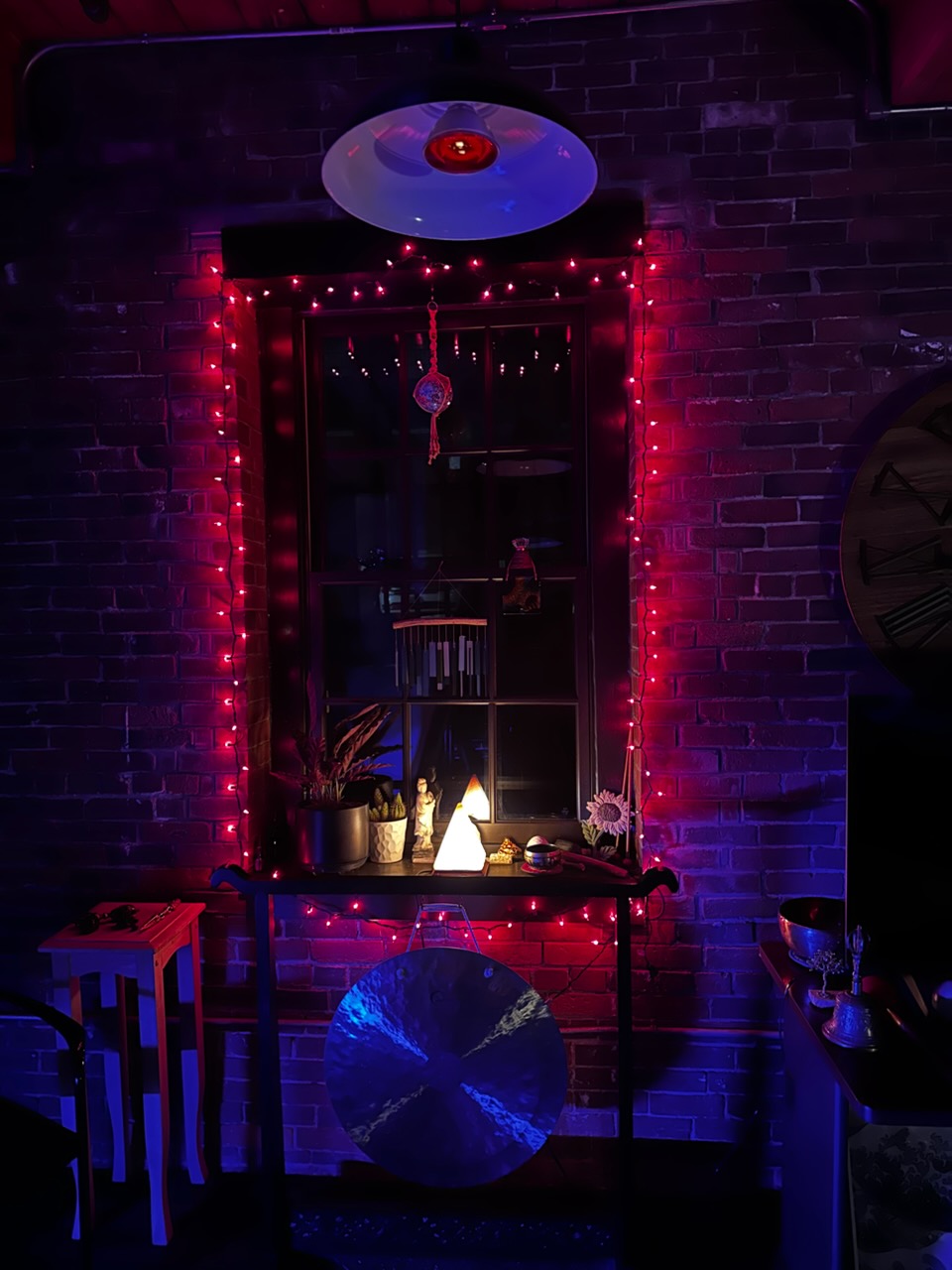 A window altar with red string lights, salt lamp, and small sound bowls